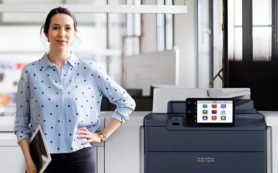 Une femme se tient à côté de l'imprimante Xerox® PrimeLink® série C9200 dans un environnement de bureau moderne
