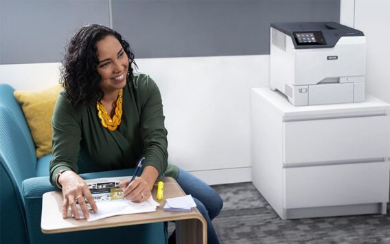 Une femme souriante dans un bureau, à côté de l'imprimante couleur Xerox® VersaLink® C620